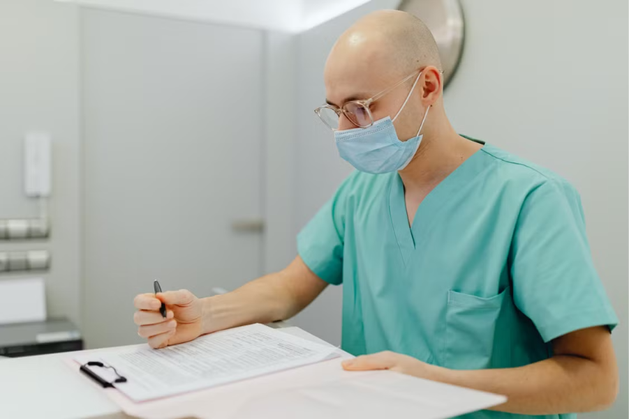 enfermeiro de máscara sentado em uma sala segurando uma caneta em cima de uma ficha médica