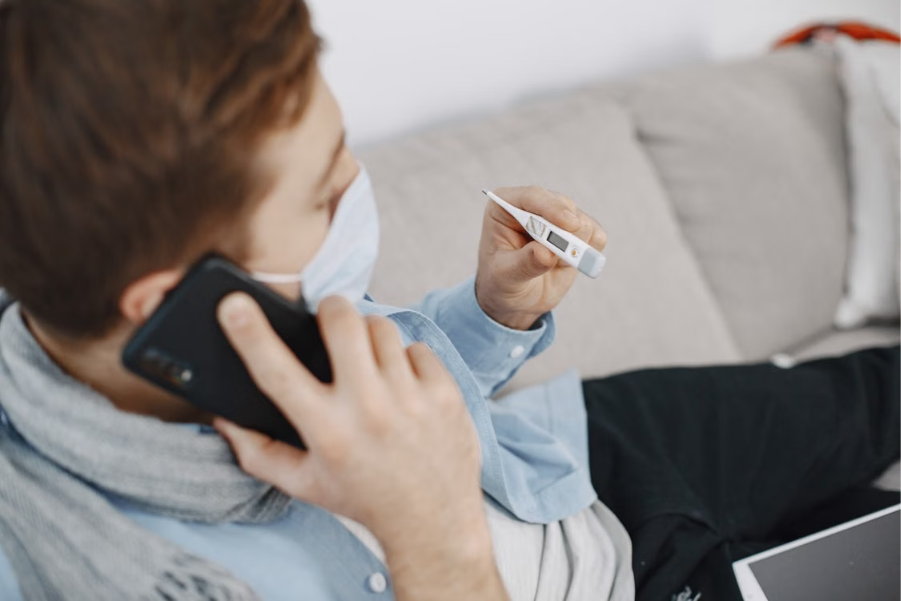 paciente sentado no sofá falando no telefone enquanto segura um termômetro