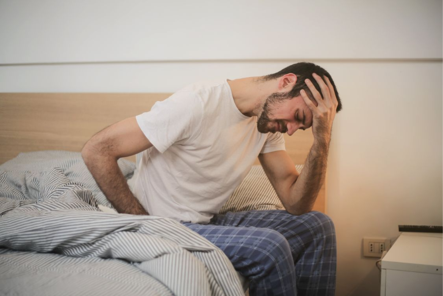 homem sentado na cama com a mão na cabeça