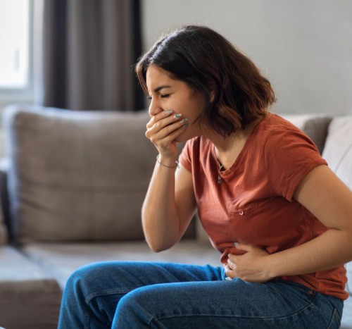 mulher sentada no sofa apertando a barriga e segurando a boca